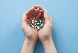 A pair of hands cupped together holds various capsules and tablets against a light blue background.
