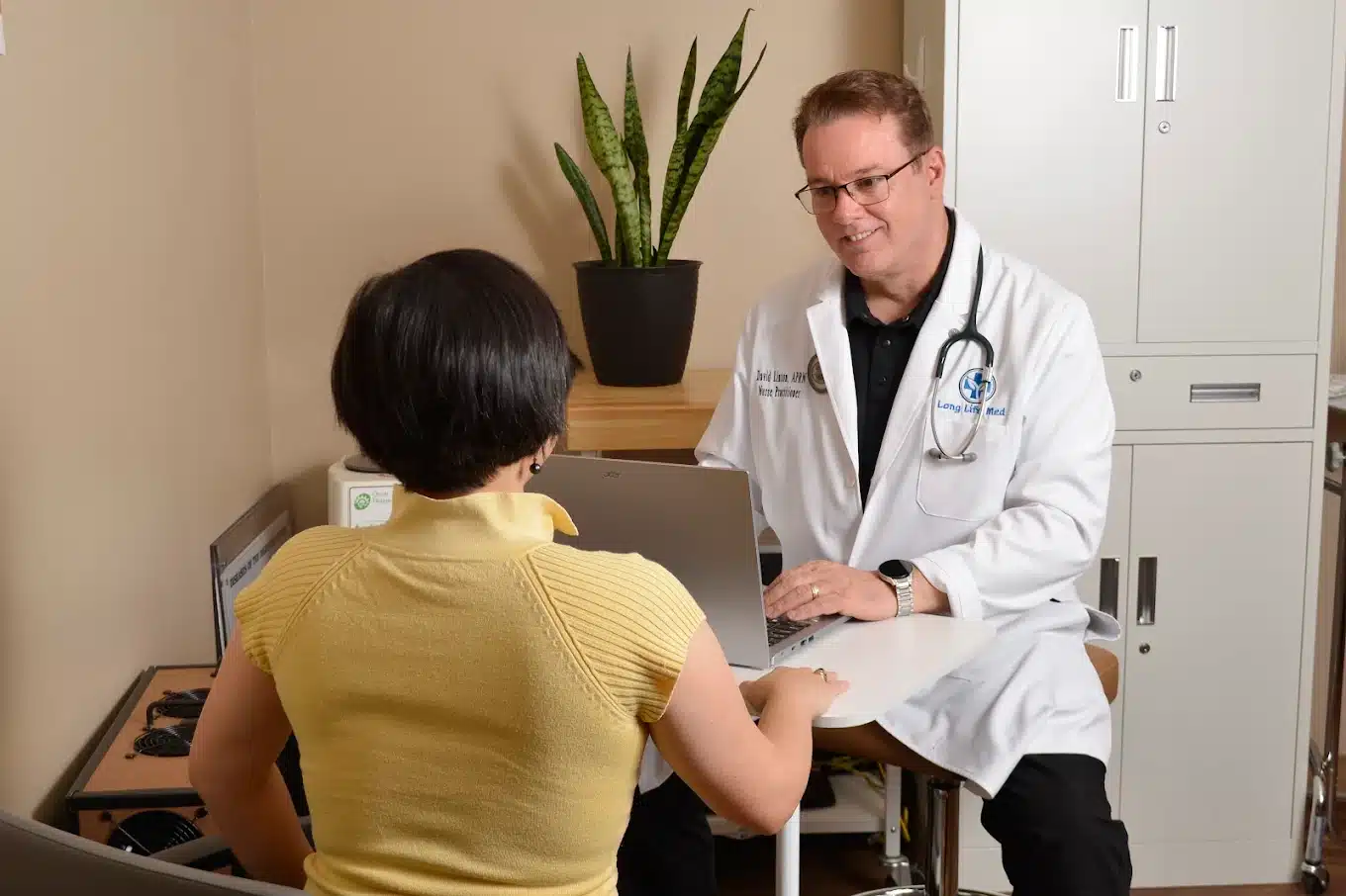 A doctor in a white coat with a stethoscope discusses functional medicine approaches with a seated patient across a desk in a medical office.